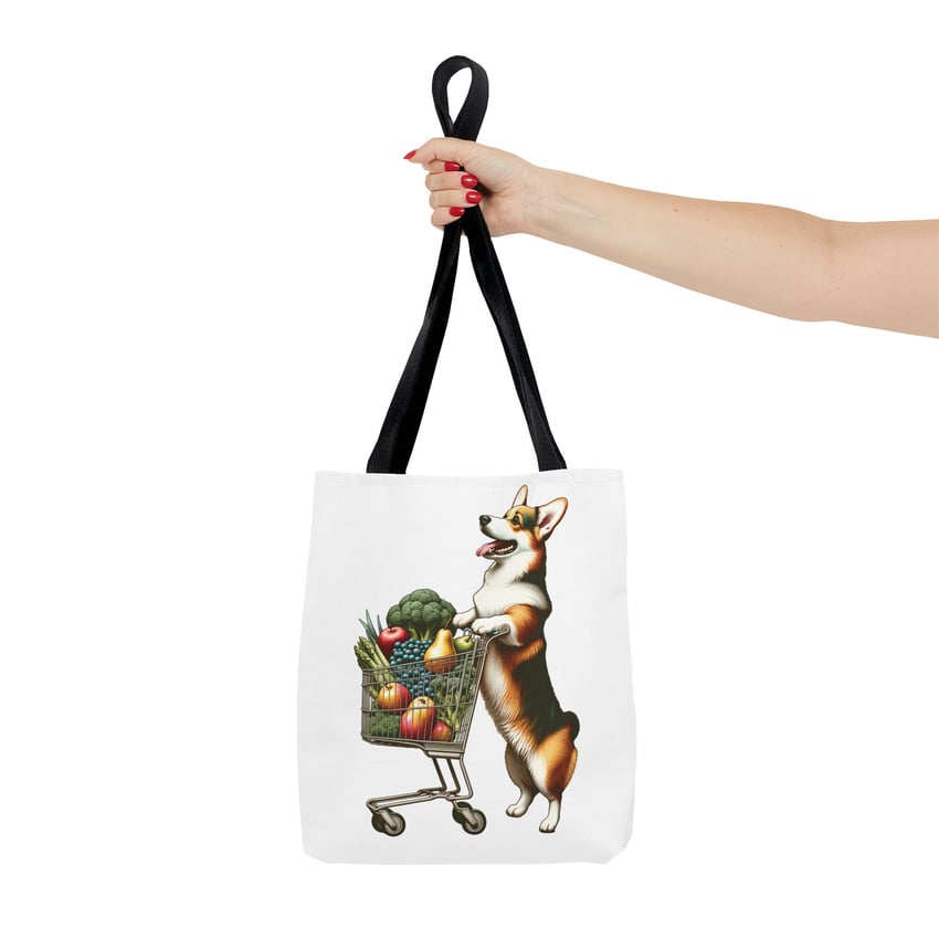 Tote bag with corgi pushing shopping cart, vibrant design, held by manicured hand.