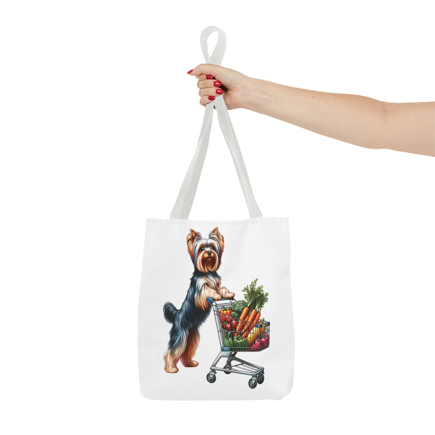 Red-nailed hand holds tote bag with Yorkshire Terrier and veggie cart illustration.