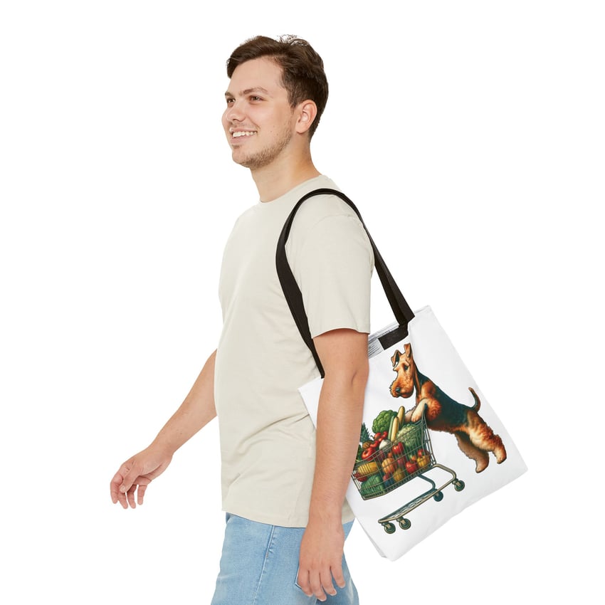 Young man in casual attire with playful dog-designed tote bag, smiling against white background.