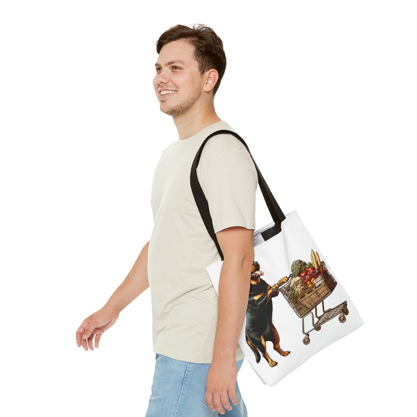 Young man smiles, carrying tote with playful Rottweiler shopping design on plain background.